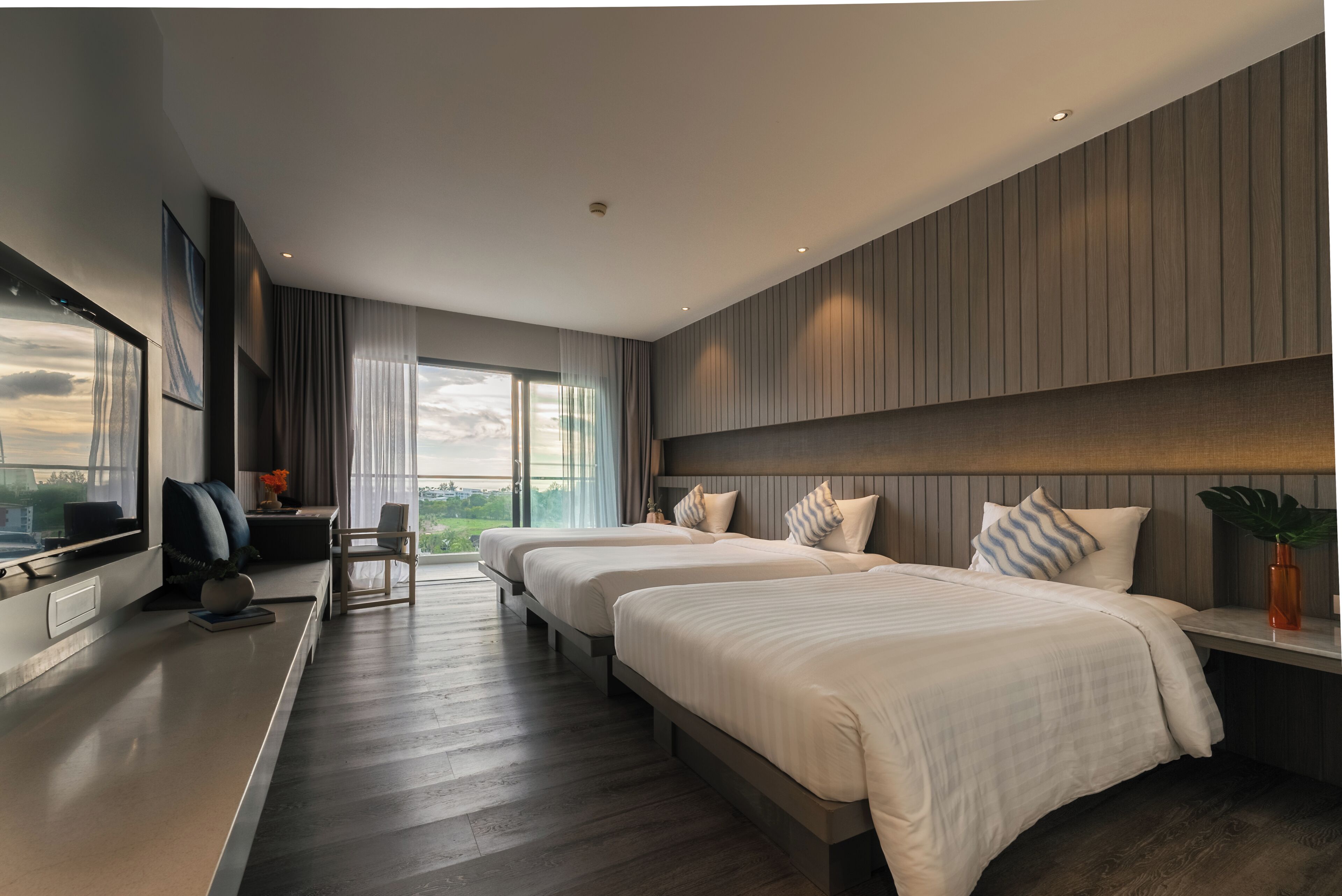 Habitación de hotel moderna con dos camas, un escritorio y un amplio ventanal con vistas a la ciudad.