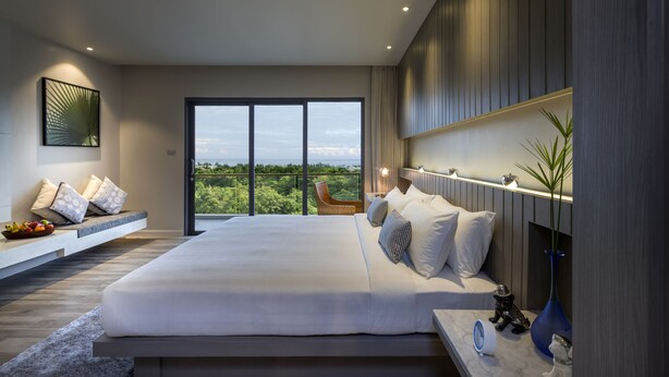 A modern bedroom with a large bed, a view of greenery, and a built-in bench with pillows.