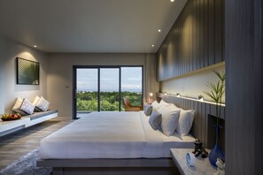 A modern bedroom with a large bed, a view of greenery, and a built-in bench with pillows. - Hotel IKON Phuket (Karon)