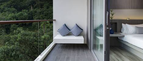 Un balcón con un banco blanco, dos almohadones estampados y una cama con ropa de cama blanca.