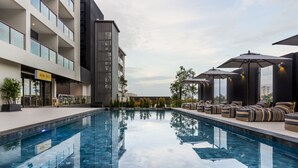 A modern hotel with a swimming pool, outdoor seating, and a visible cafe.
