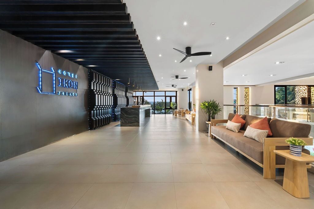 A modern hotel lobby with a reception desk, seating area, and a staircase.
