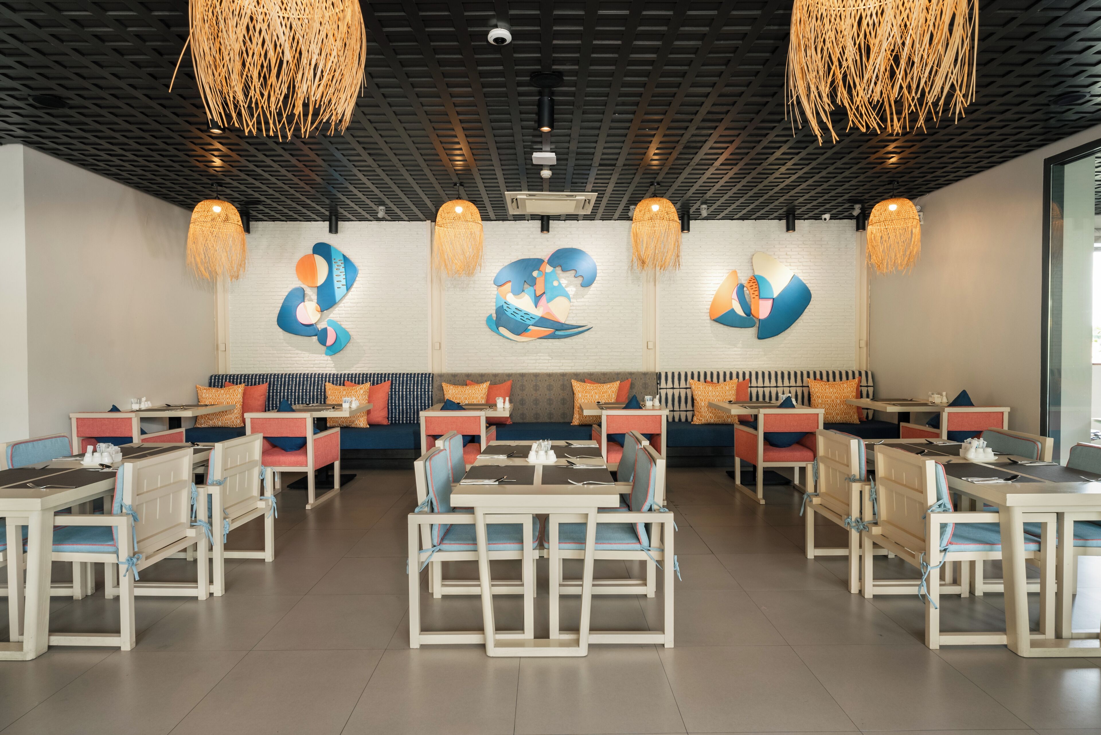 A modern restaurant with white and blue furniture, hanging woven light fixtures, and abstract wall art.