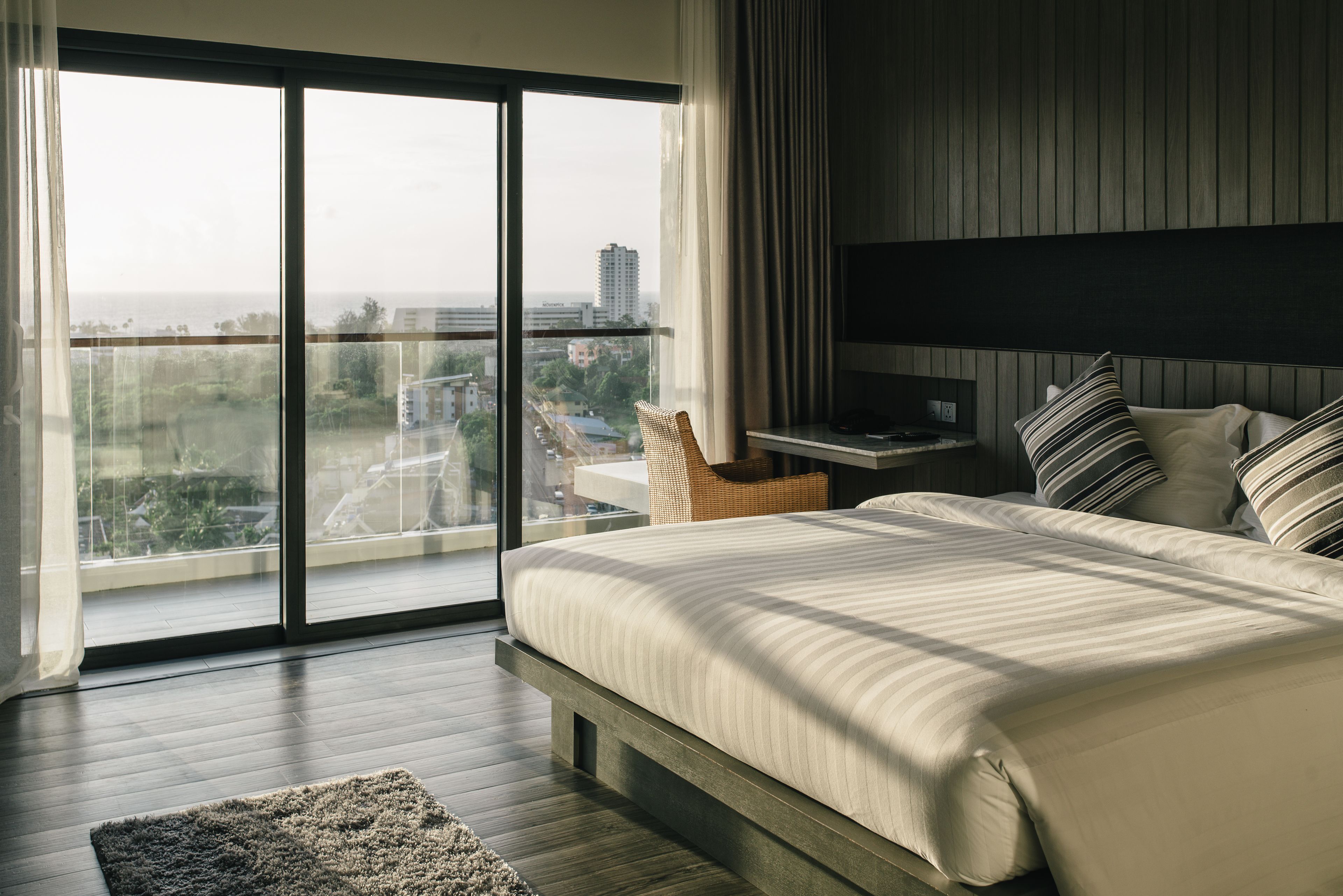 A modern bedroom with a large bed, a nightstand, a TV, and a view of the city through a large window.