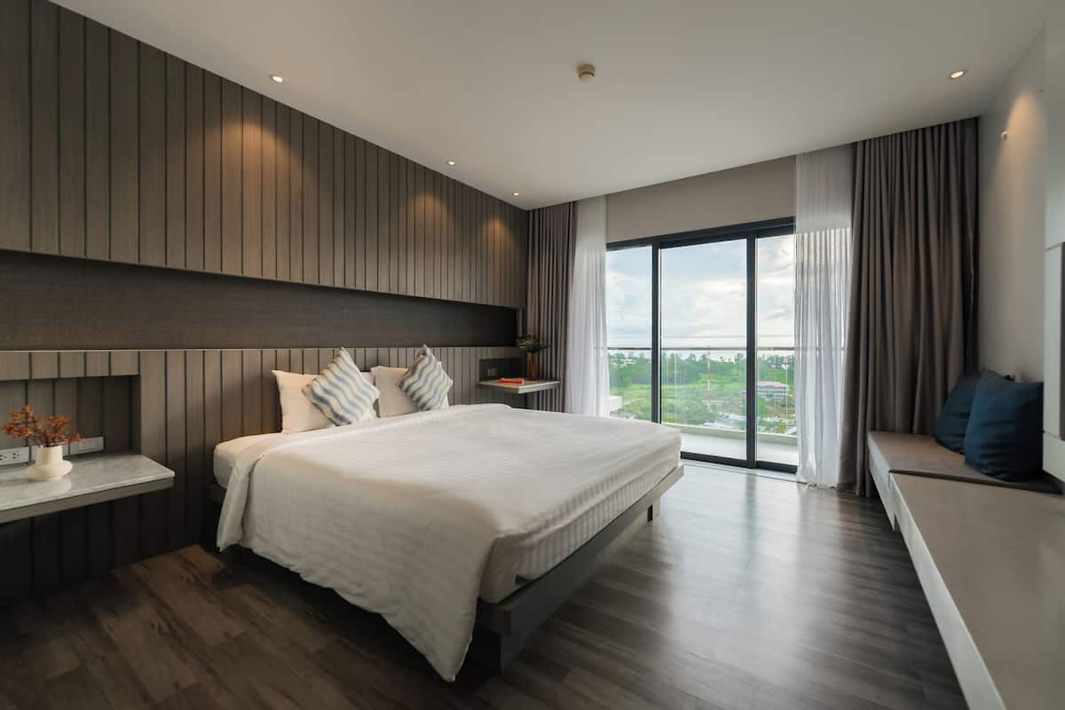 Une chambre moderne avec un grand lit, une table de chevet, une commode et une vue sur l’extérieur grâce à une grande fenêtre.