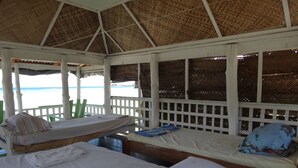 Una cabaña frente al mar con dos camas, techo de paja y vista al océano.