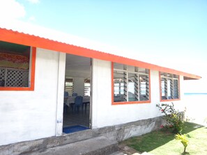 A building with a red roof and white walls, featuring a door leading to an interior with blue chairs and a table. - Tailua Beach Fale (Manase)