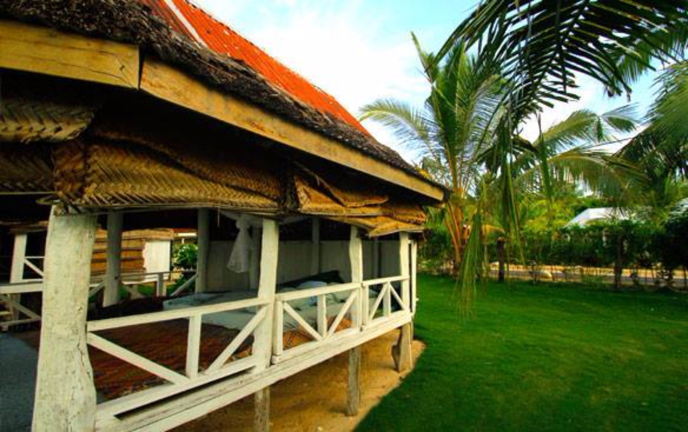 A thatched-roof structure with a covered outdoor seating area, surrounded by lush greenery and palm trees.