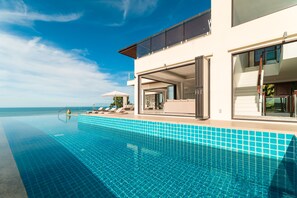 Una piscina infinita moderna con agua azul cristalina, un edificio blanco con amplios ventanales y vistas al océano.