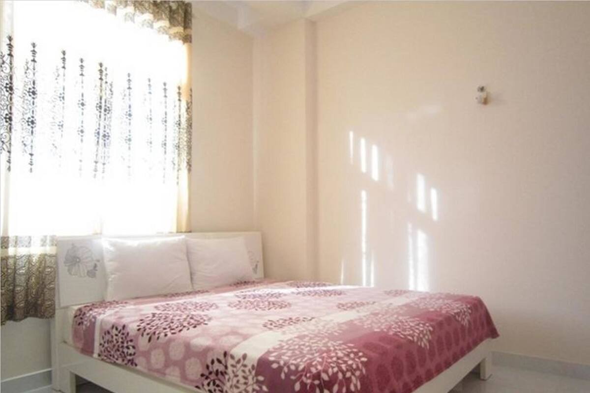 A bedroom with a bed, white walls, and a window with curtains.