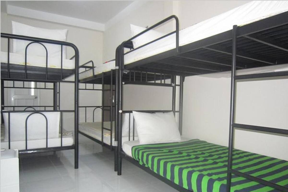 A bunk bed room with a metal frame, white bedding, and a green striped mattress cover.