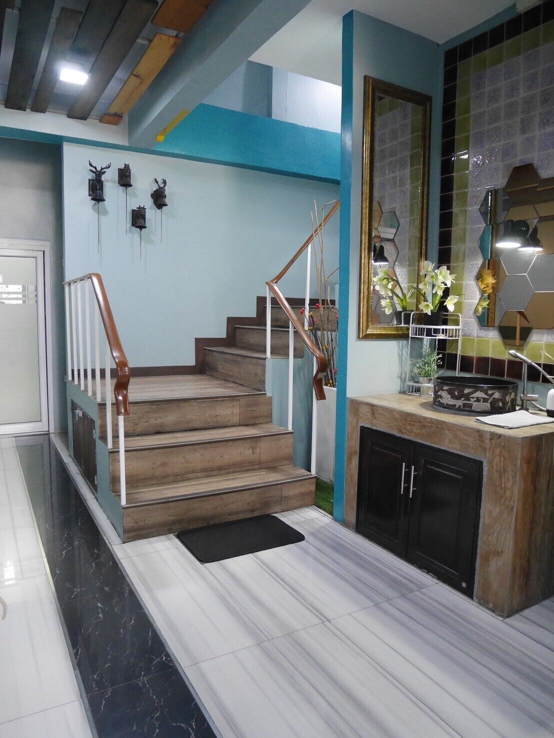 Una escalera con escalones de madera y barandilla de metal que conduce a una zona de cocina con salpicadero de azulejos y encimera.