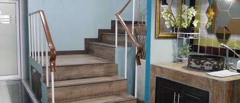 Una escalera con escalones de madera y barandilla de metal que conduce a una zona de cocina con salpicadero de azulejos y encimera.