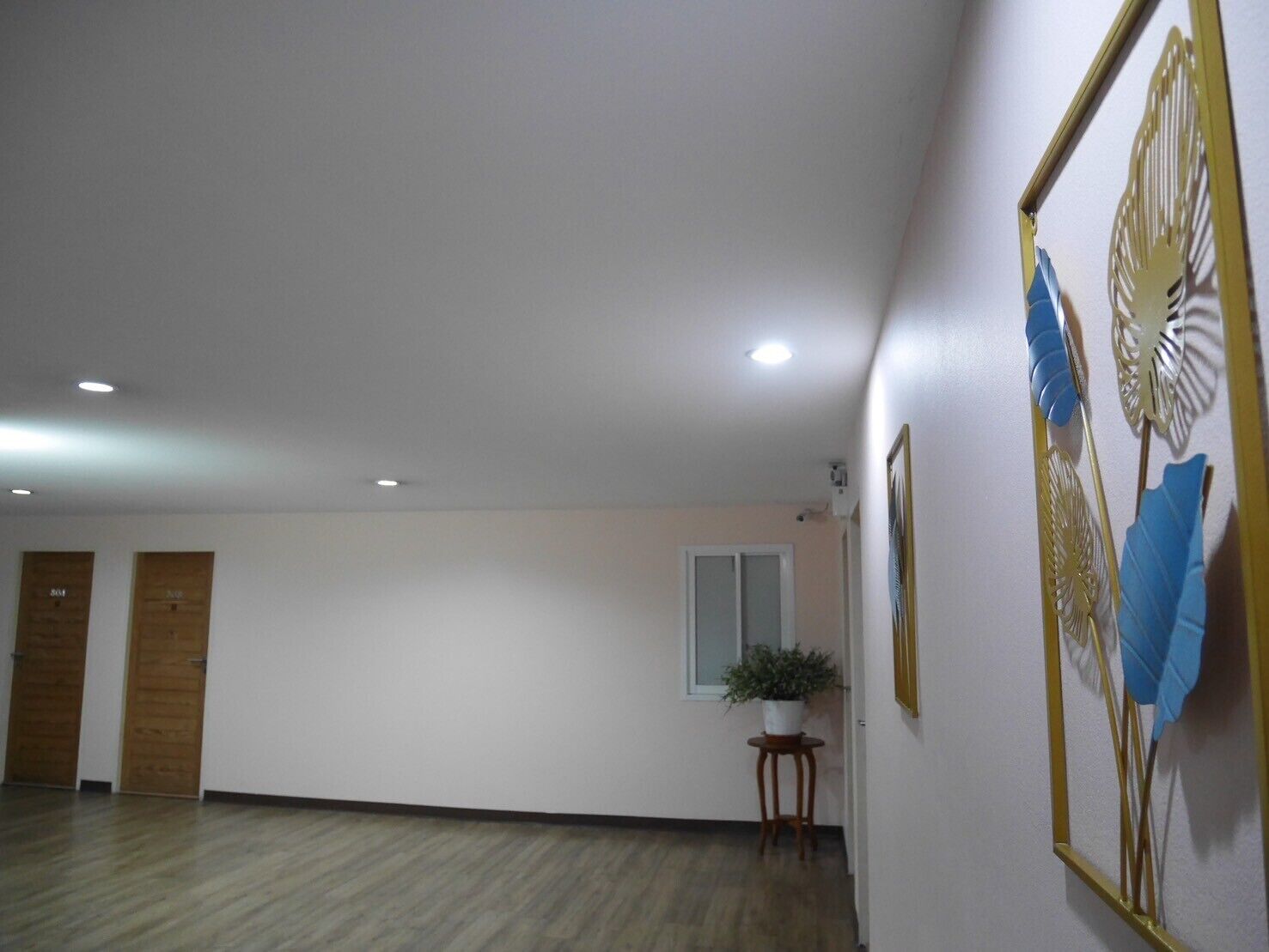 A spacious hallway with wooden flooring, a potted plant, and framed artwork on the walls.