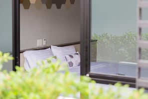 A modern bedroom with a bed, a bedside telephone, and a view of greenery outside. - M2 Hotel (Phayao)