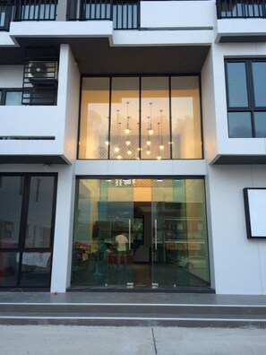 A modern building with large glass windows, a visible interior with a staircase, and a series of hanging lights. - M2 Hotel (Phayao)