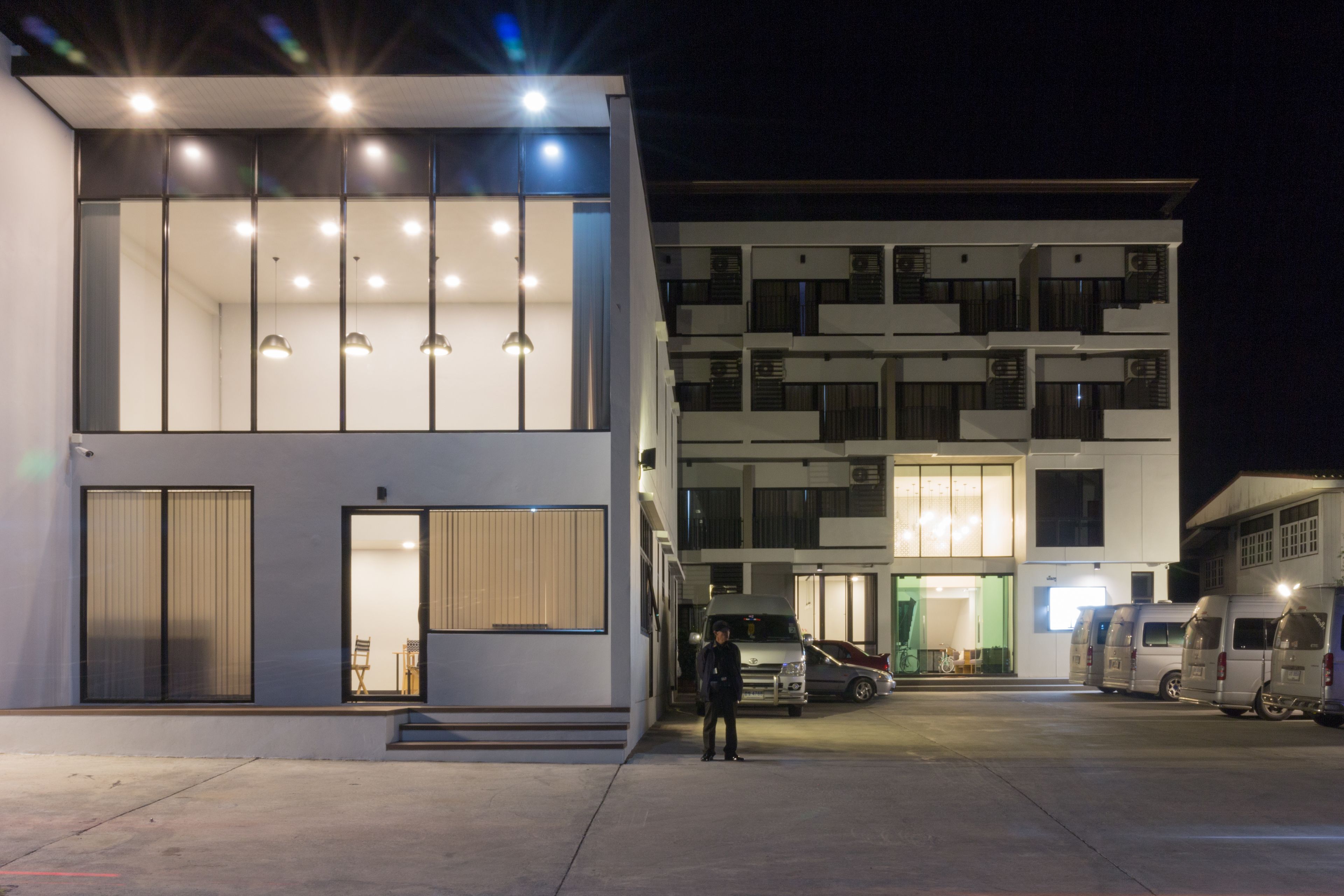 Een modern gebouw met een tweelaags ontwerp, grote ramen en een parkeerplaats met verschillende voertuigen.