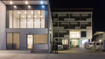 Um edifício moderno com estrutura em dois andares, grandes janelas e um estacionamento com vários veículos.