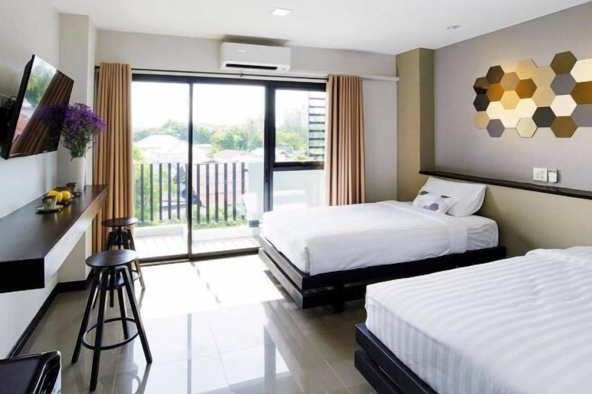 A hotel room with a balcony, a TV, a desk with stools, and a bed.