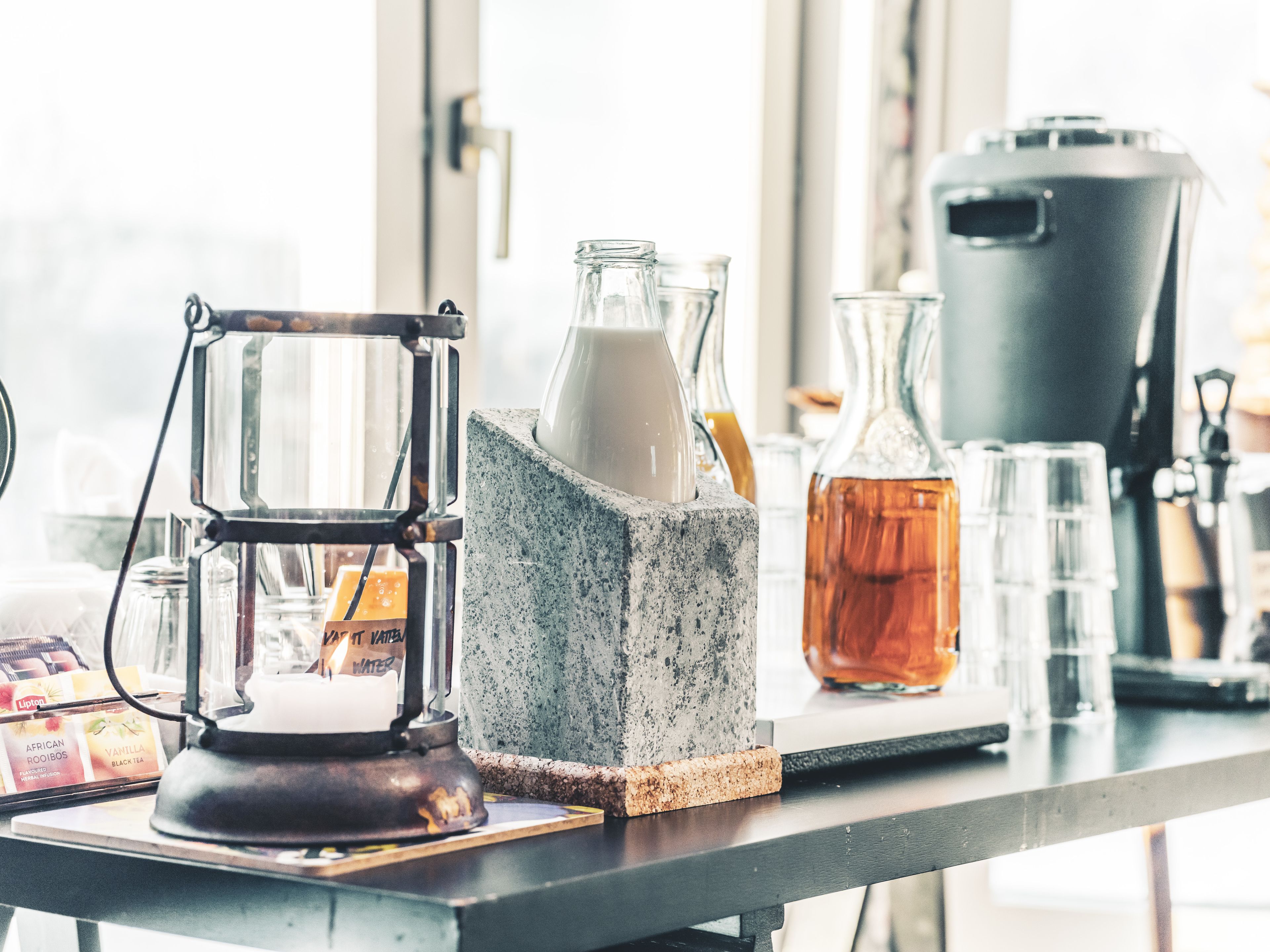 Una encimera de cocina con una cafetera francesa, una jarra de leche, una olla grande y varias botellas de vidrio.