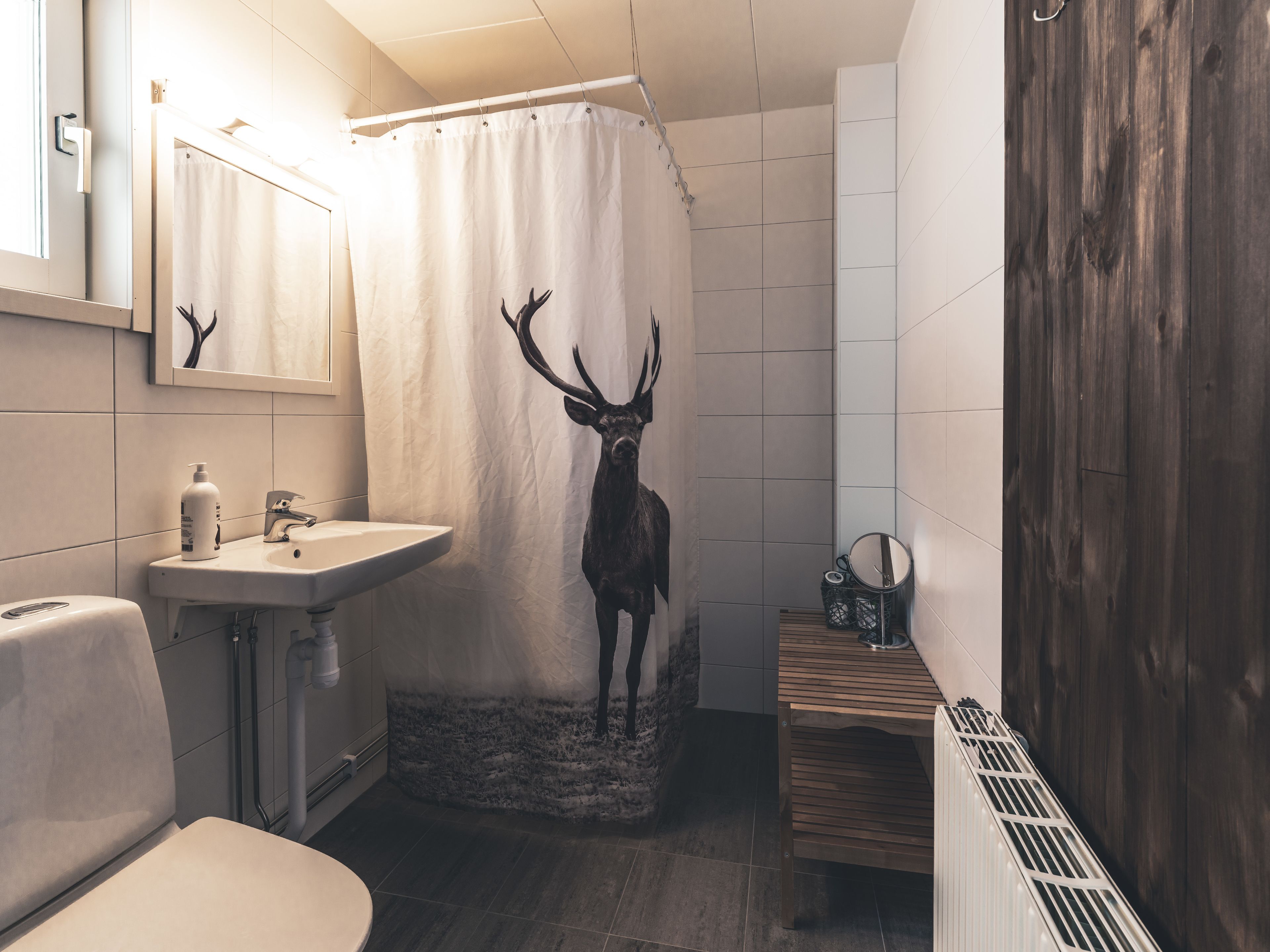 Un baño con cortina de ducha con ciervo, lavamanos, espejo y radiador.