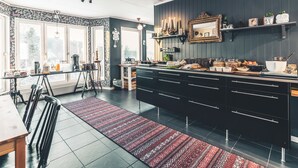 A modern kitchen with dark cabinetry, a central island, and a dining area with a red patterned rug. - Åre Bed & Breakfast (Are)