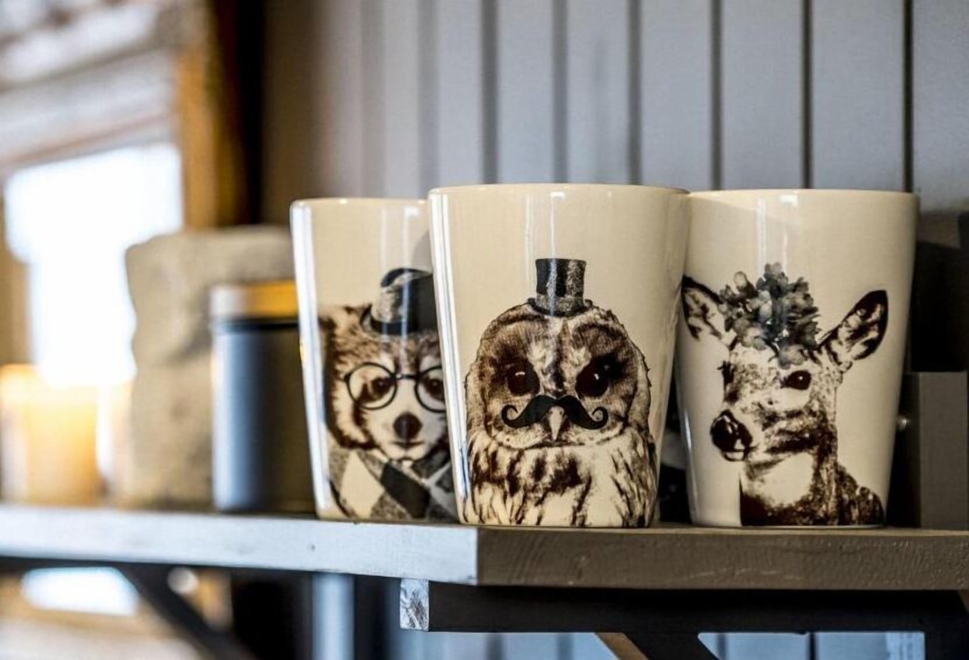 Three ceramic mugs with animal designs on a shelf.