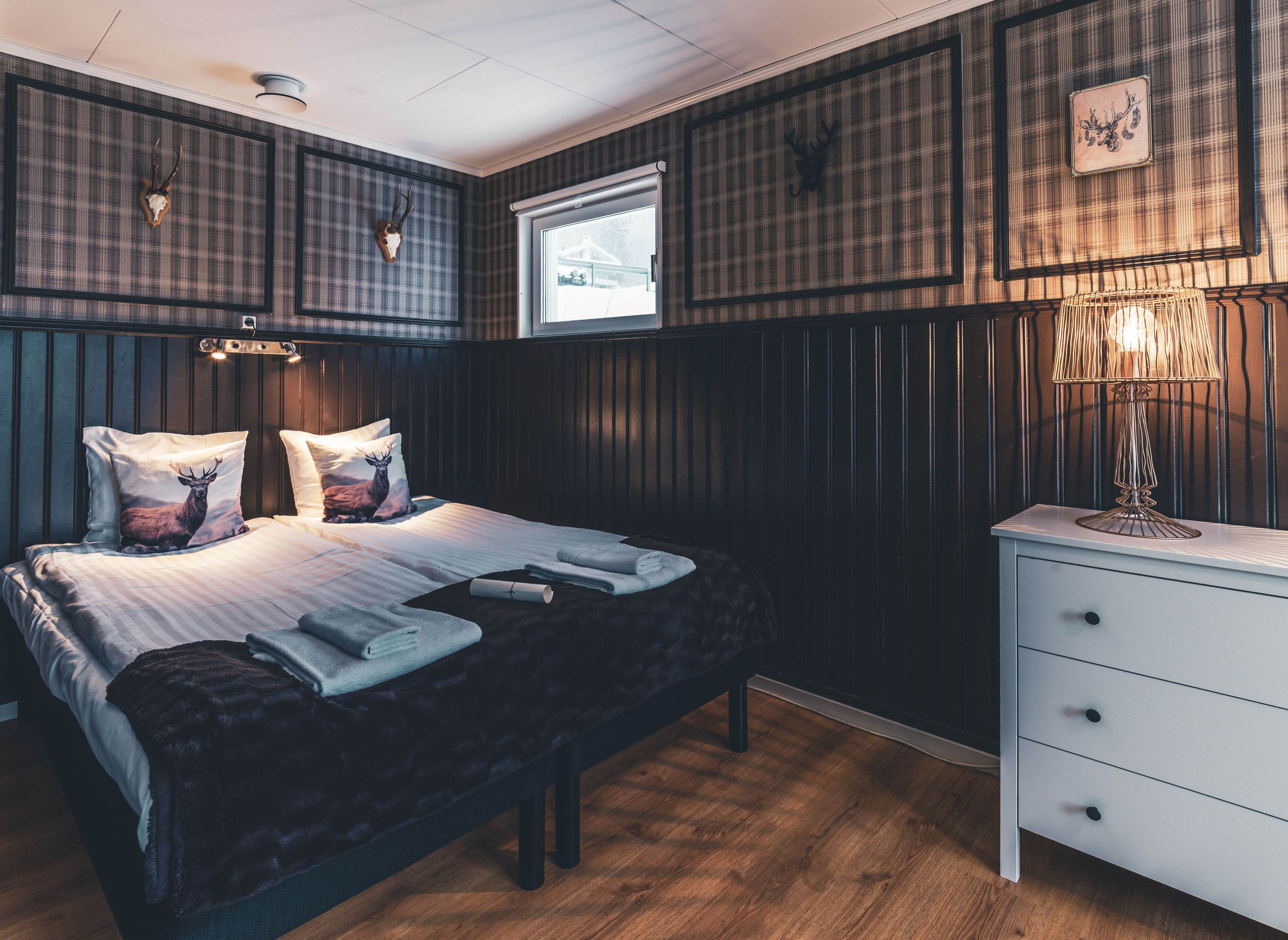 A bedroom with a bed, pillows, a bedside table, a lamp, and a window.