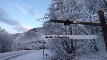 A sign indicating a bed and breakfast with a snowy landscape and a mountain in the background.