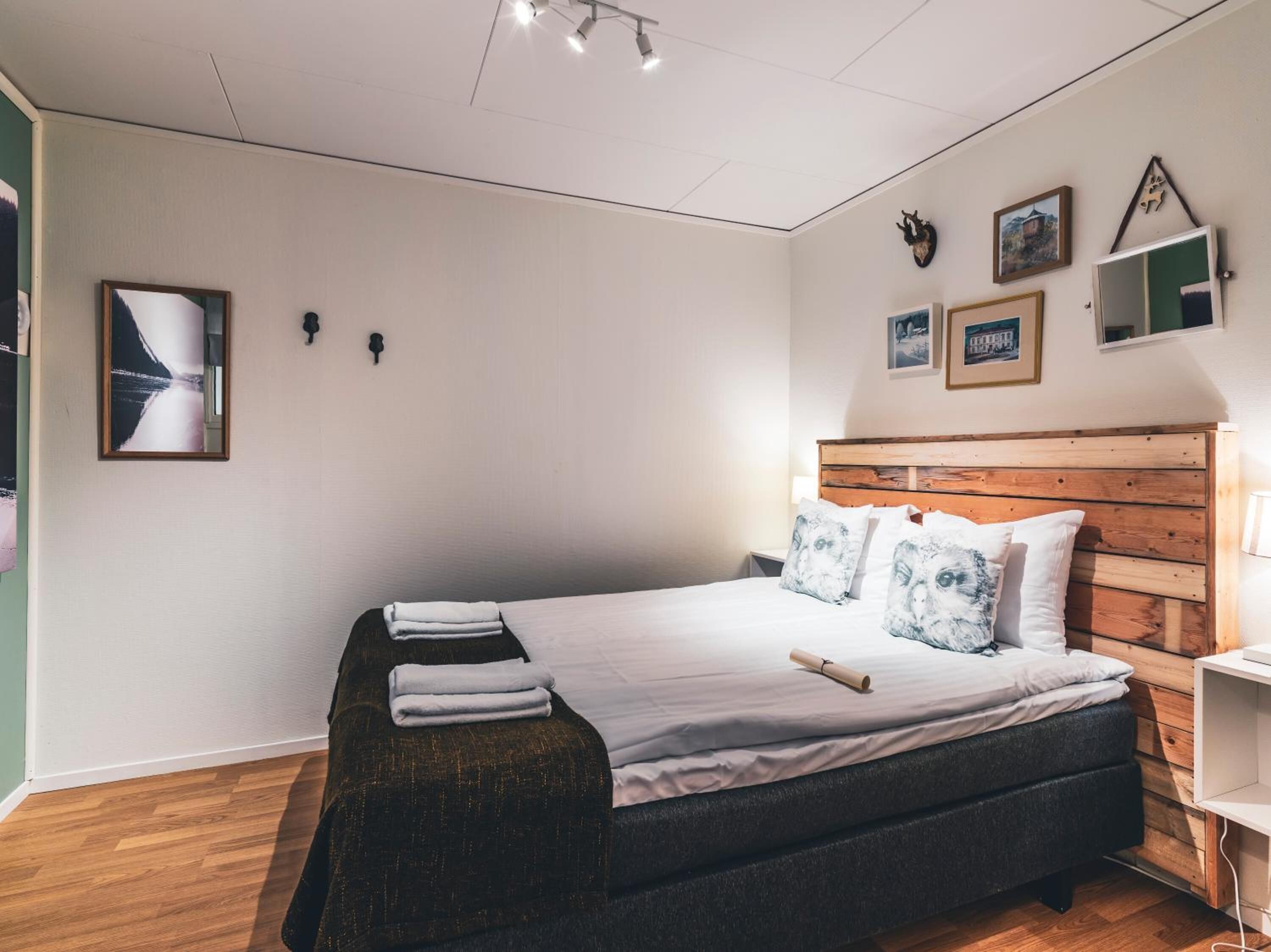 A neatly arranged bedroom with a wooden headboard, a bed with white linens, a bedside table, and a wall-mounted TV.