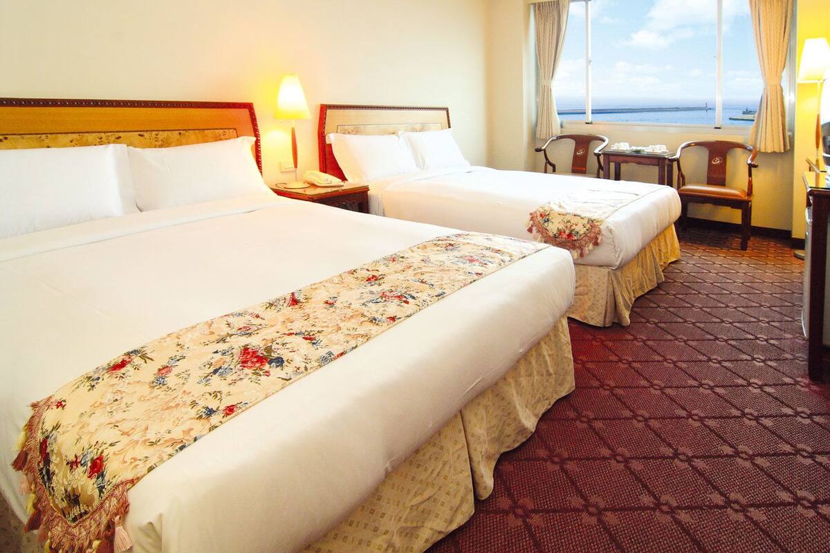 Habitación de hotel con dos camas, un escritorio y vista al mar.
