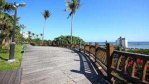 A wooden boardwalk with benches, palm trees, and a view of the ocean. - Ola Hotel (Hualien City)
