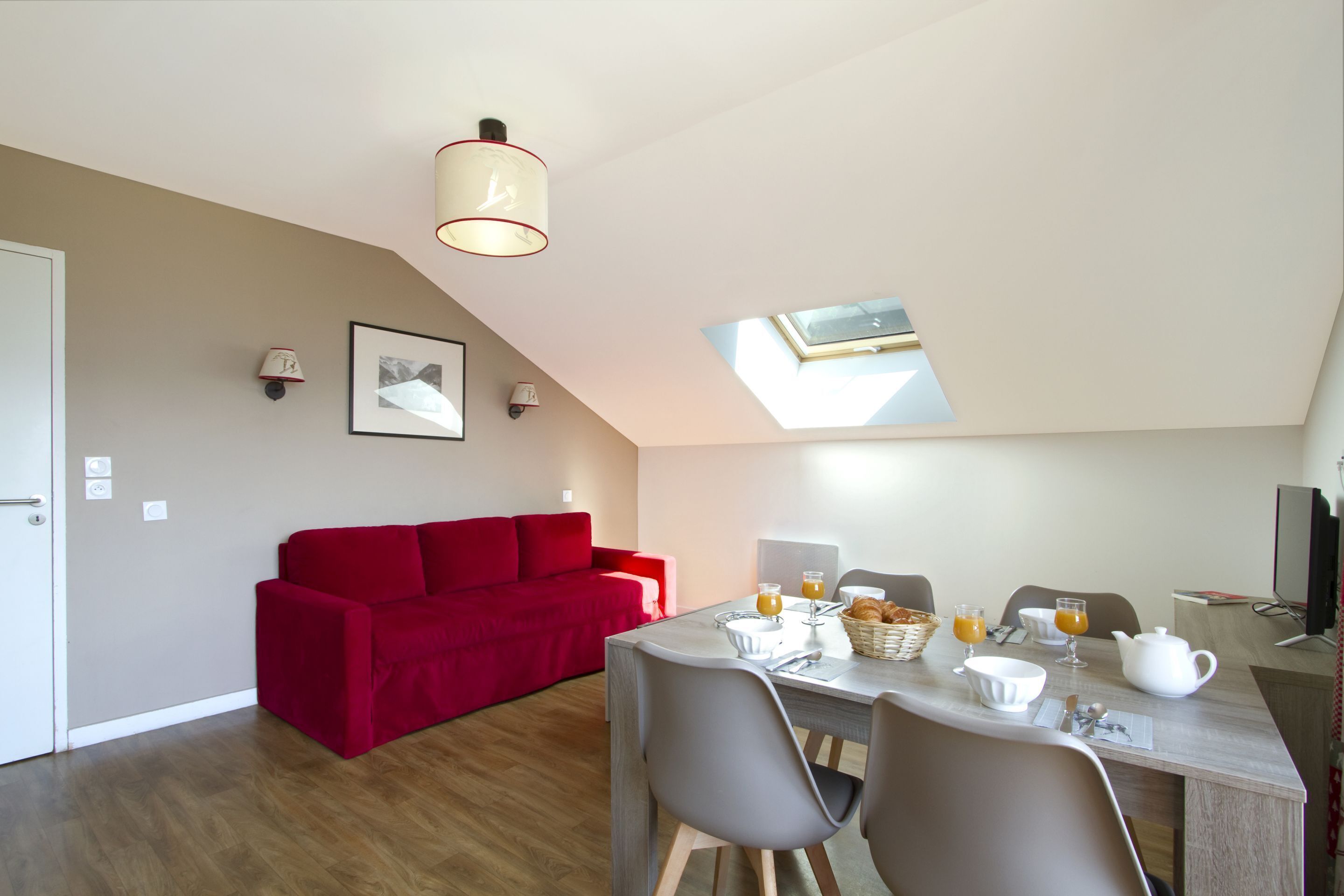 A modern room with a dining table set for breakfast, a red sofa, and a skylight.