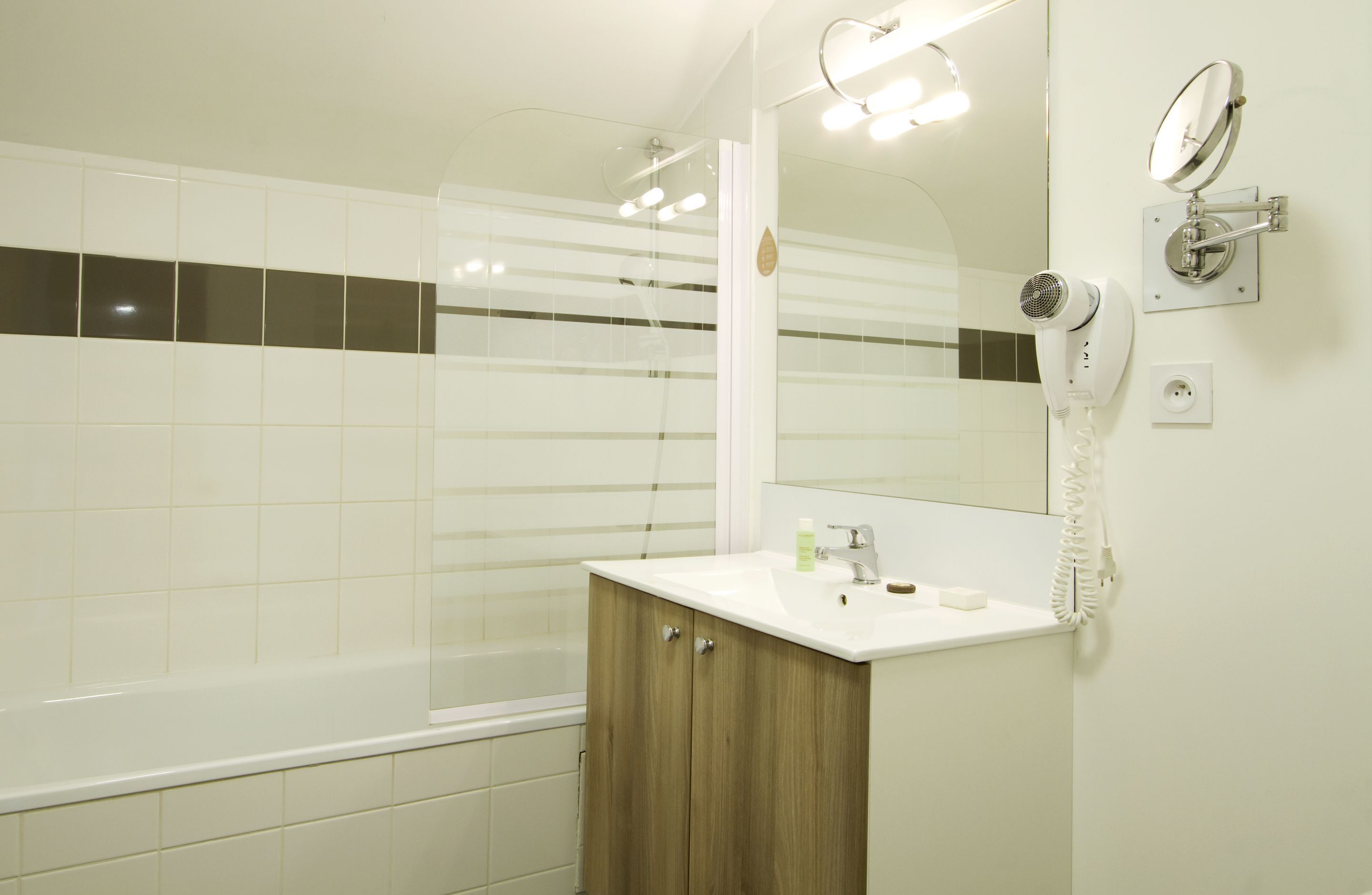 A modern bathroom with a bathtub, a vanity with a mirror, and a hairdryer mounted on the wall.