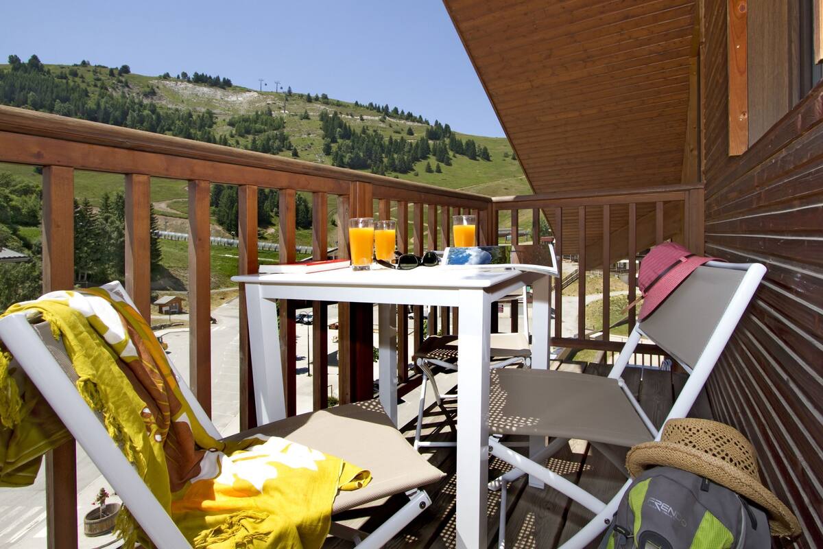 A balcony with a table, chairs, and a view of a green hillside.