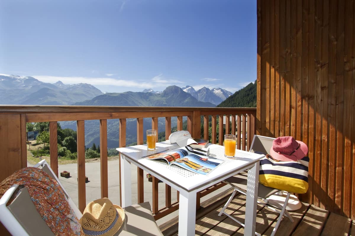 A wooden deck with a table set for two, featuring a magazine, a laptop, and glasses of orange juice.