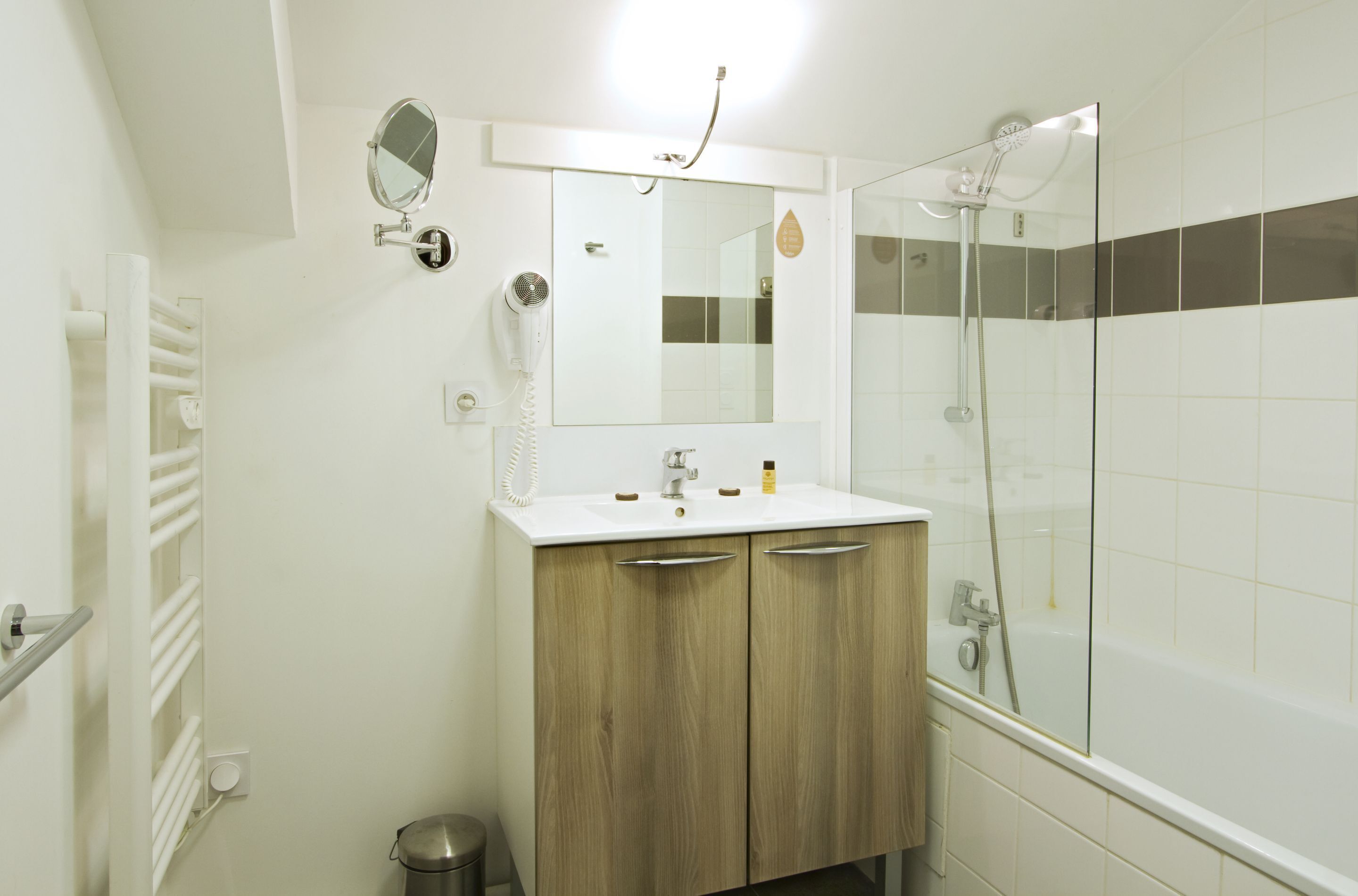 A bathroom with a white sink, wooden cabinets, a mirror, a hairdryer, and a glass-enclosed shower.
