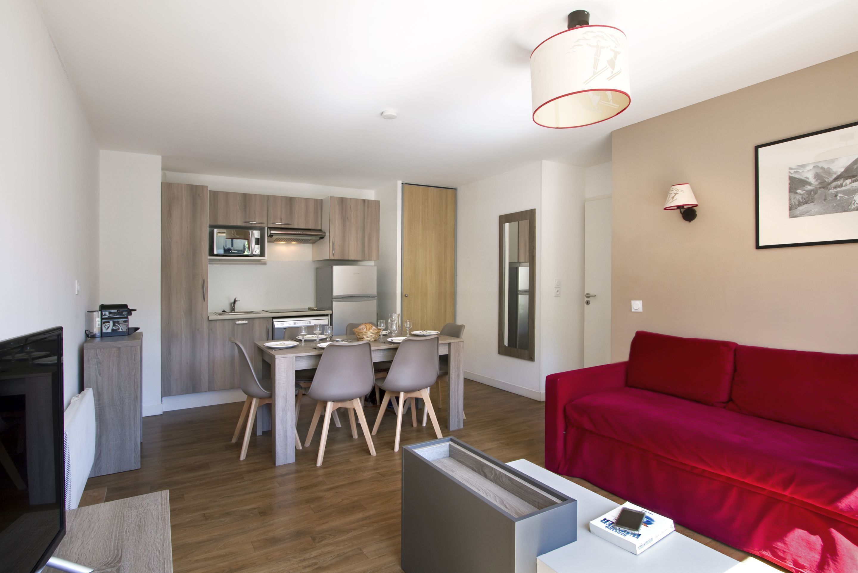 A modern living room with a red sofa, a dining area with a table and chairs, and a kitchen with wooden cabinets and a microwave.