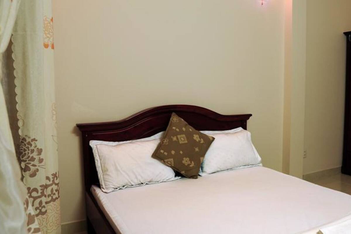 A neatly made bed with white linens and a brown patterned pillow in a room with a wooden headboard.