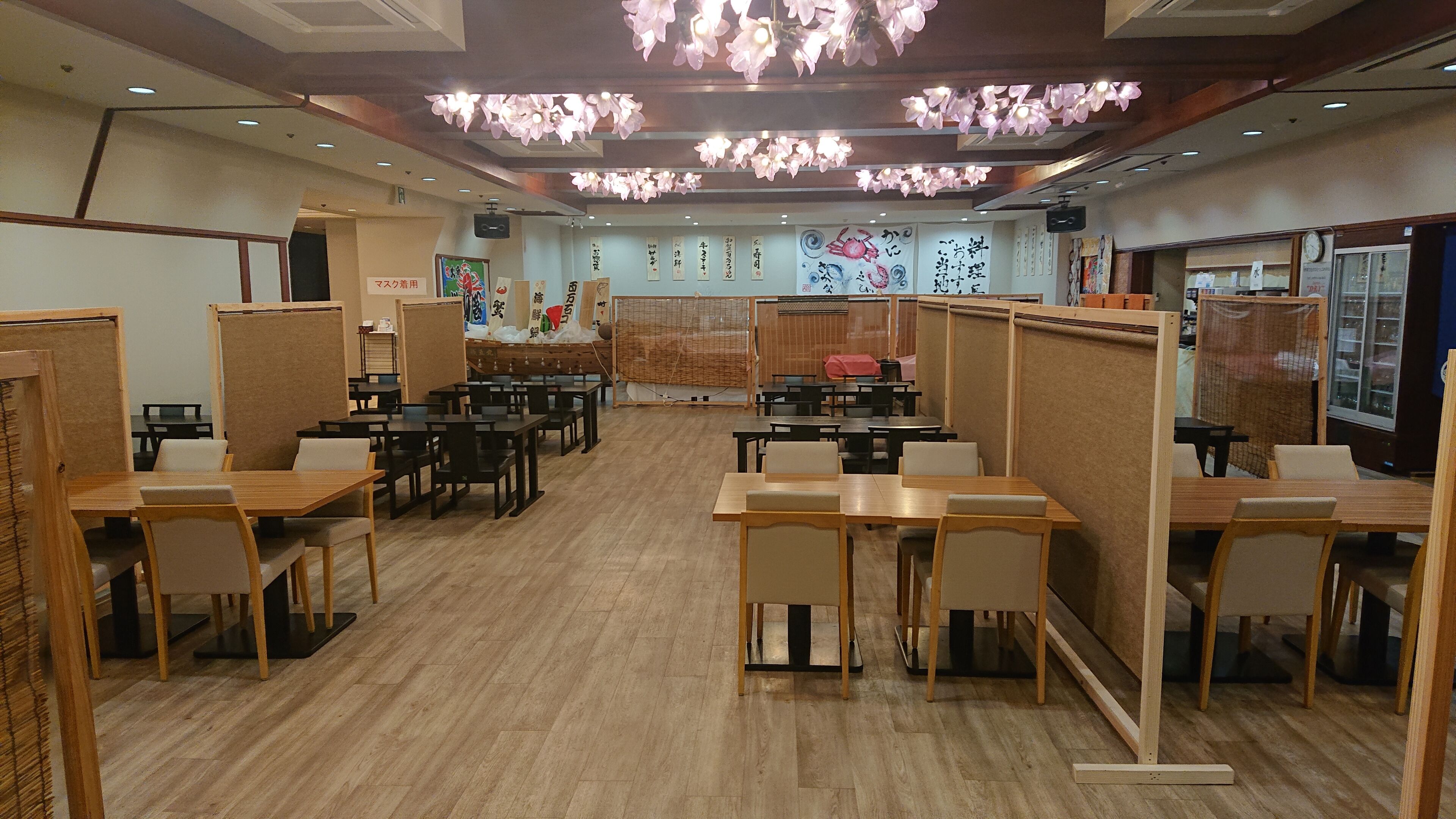 A restaurant with wooden tables and chairs, partitioned booths, and decorative ceiling lights.