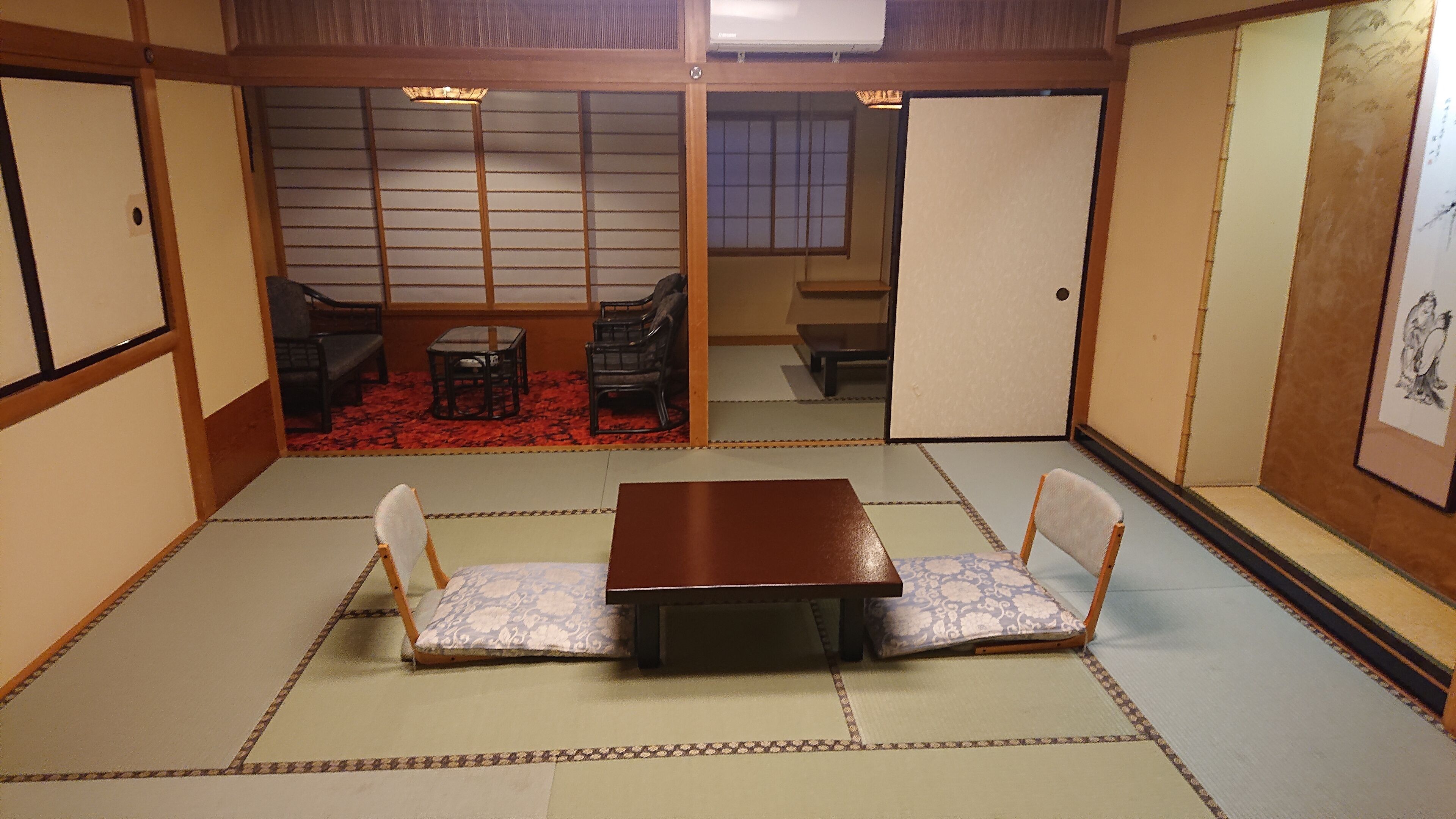 A traditional Japanese room with tatami flooring, a low wooden table, and two tatami mats with cushions.