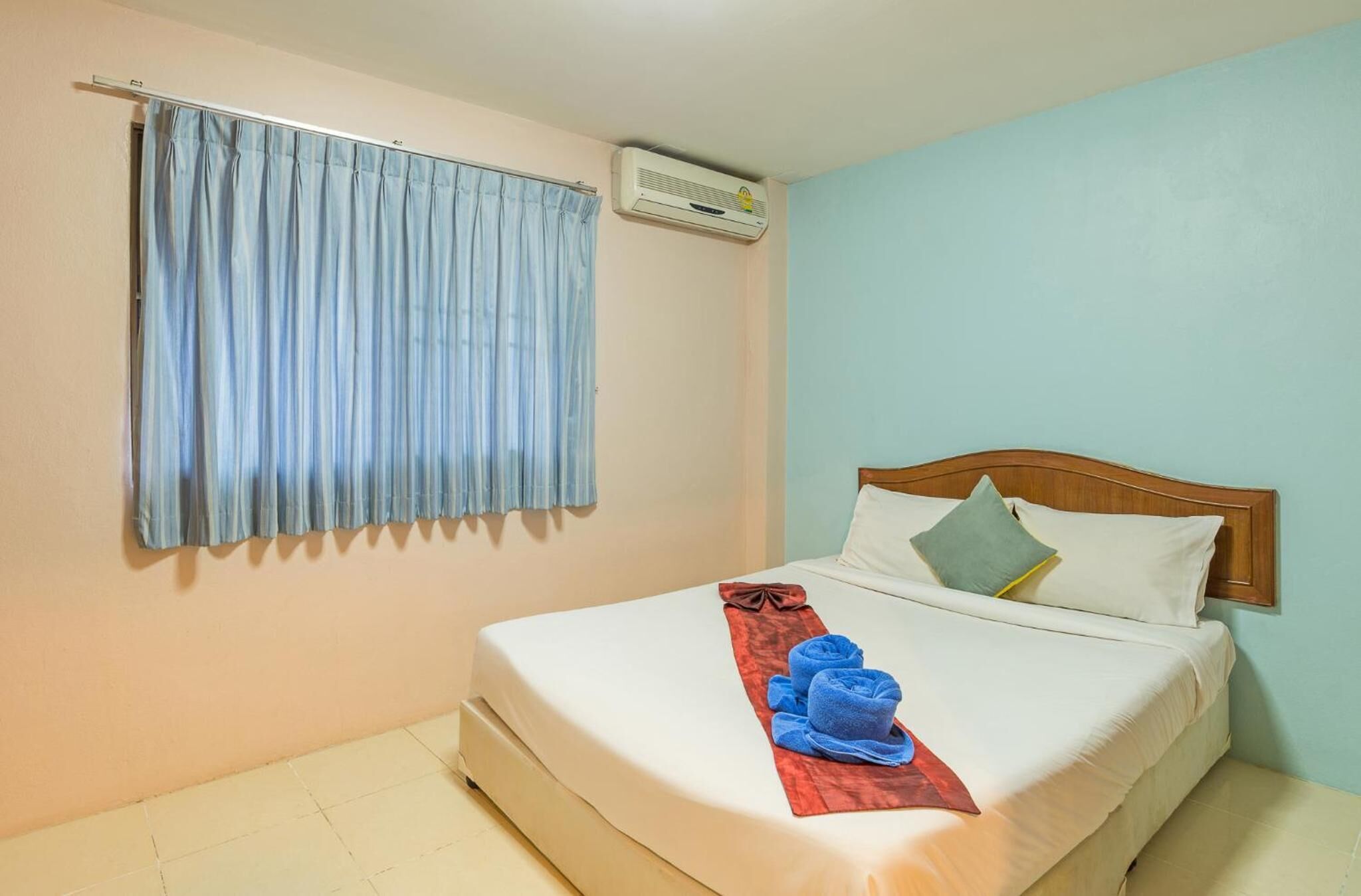 A hotel room with a bed, a window with curtains, an air conditioning unit, and a towel rack with towels.