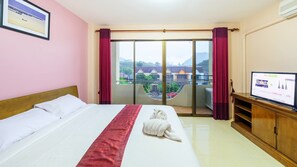 Habitación de hotel con cama, televisión, balcón con cortinas y vista a edificios.
