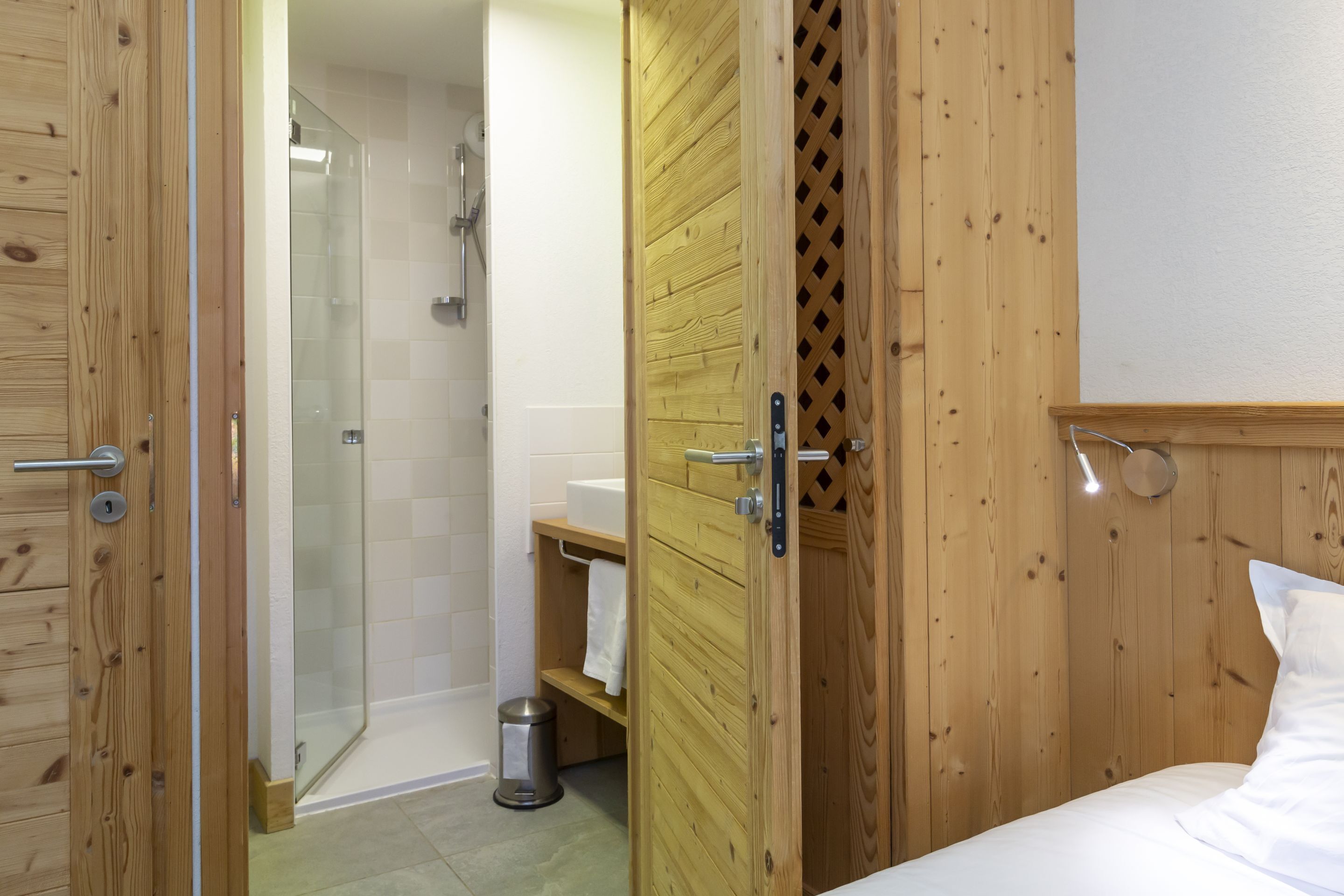 A wooden-paneled room with a shower, a sink, and a bed.