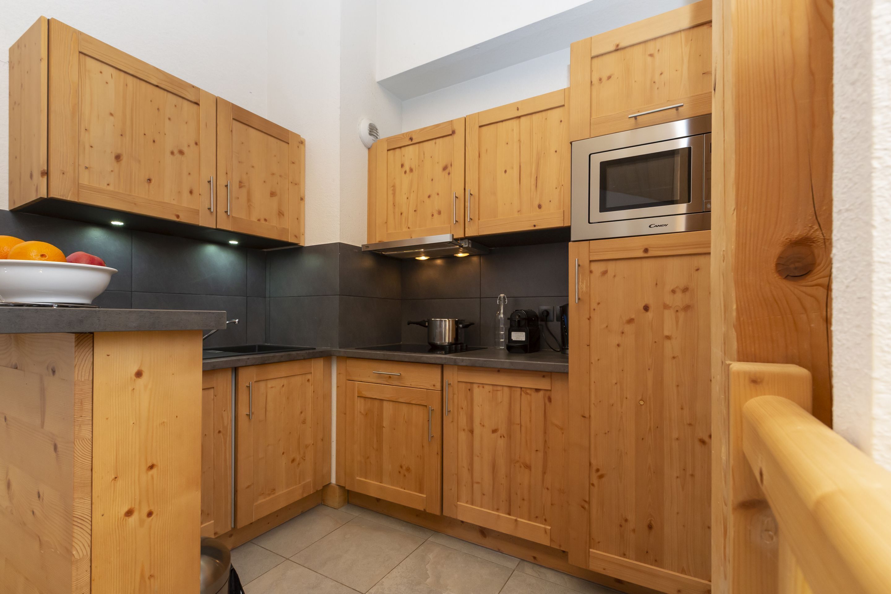 A kitchen with wooden cabinets, a microwave, and a bowl of fruit on the counter.