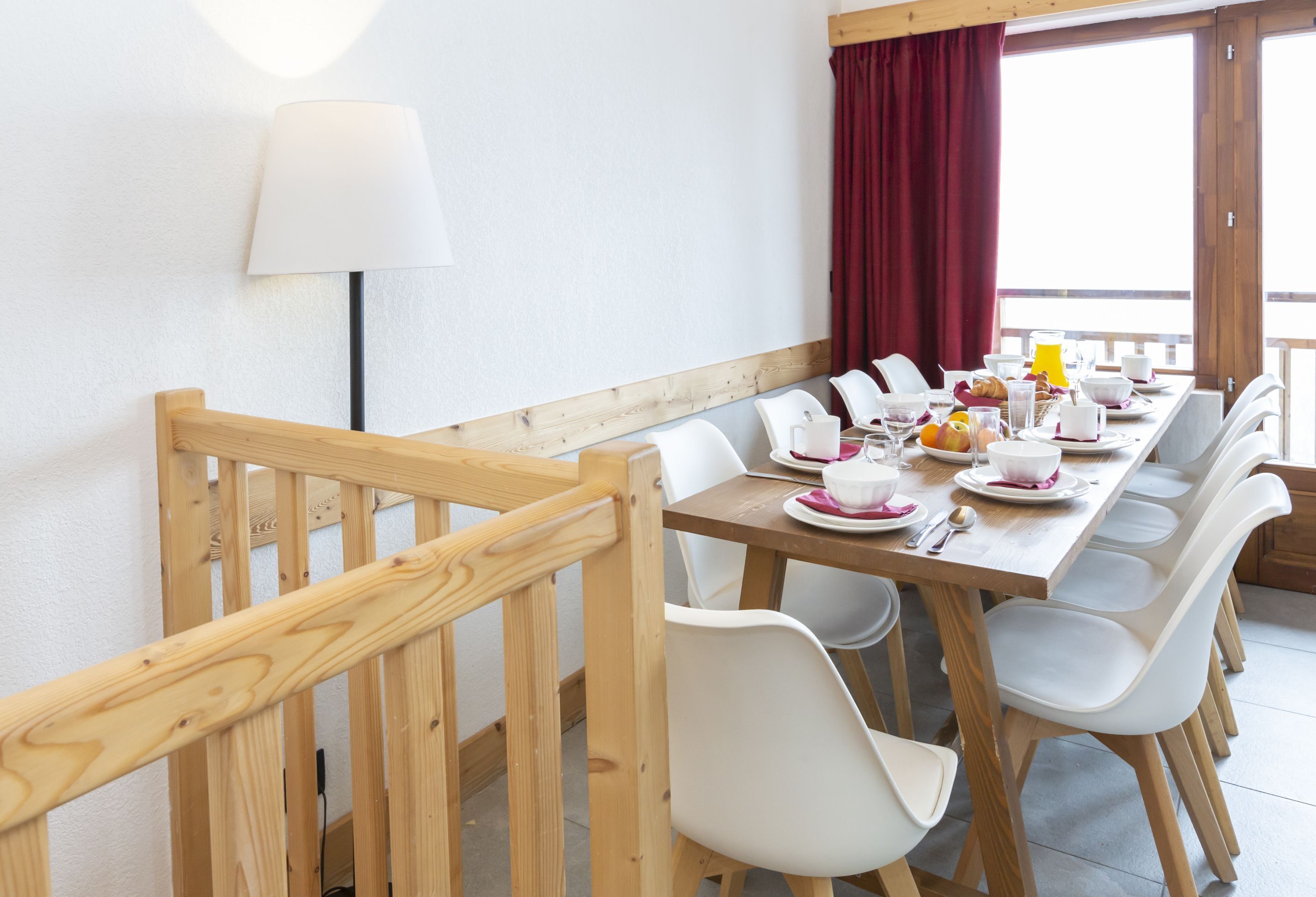 A dining area with a wooden table, white chairs, and a red curtain.