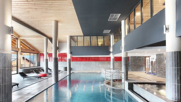 An indoor swimming pool with lounge chairs and a red wall. - Résidence Odalys Les Fermes de Chatel (Chatel)