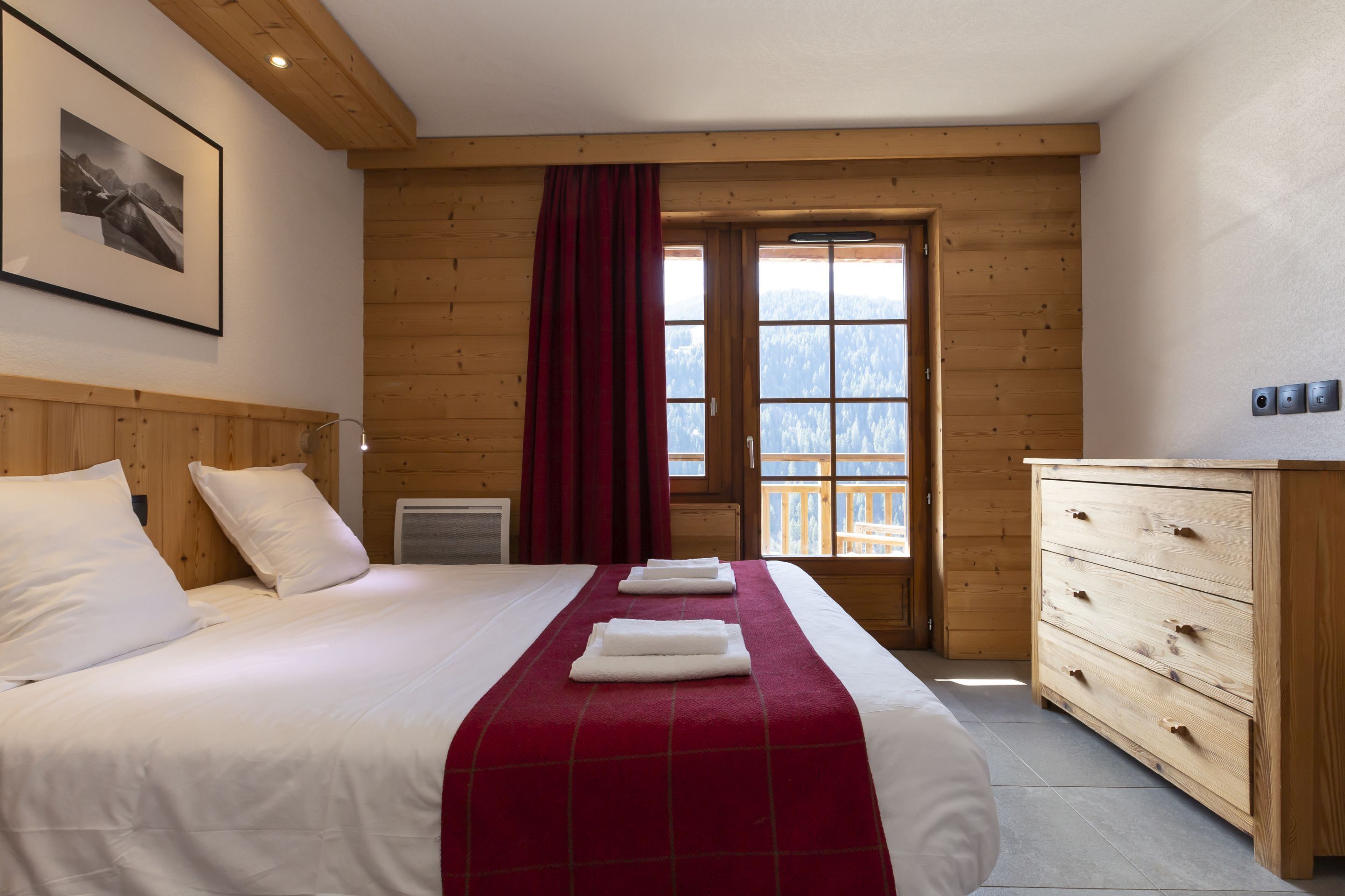 A hotel room with a bed, a wooden dresser, a window with a view, and a framed picture on the wall.