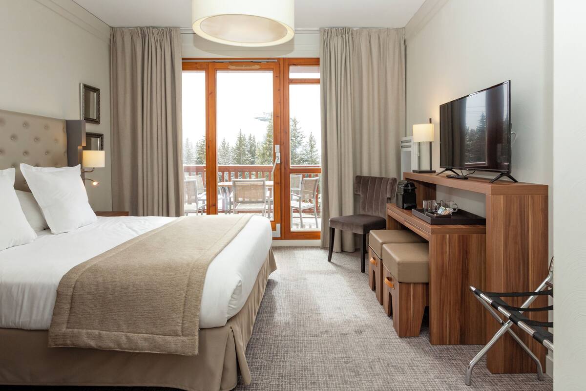 Een hotelkamer met een bed, bureau, televisie en balkon met stoelen.