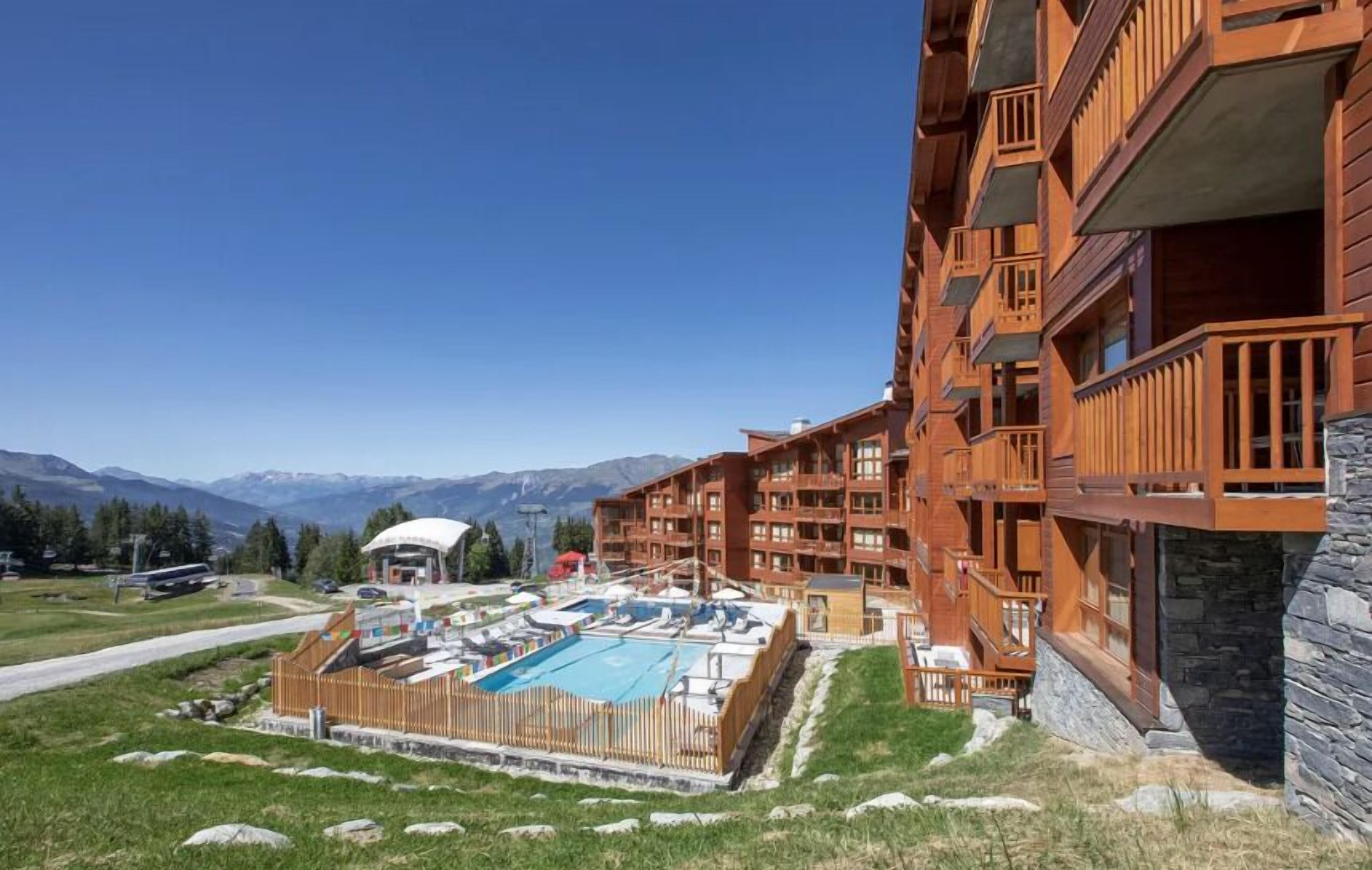 A hotel with multiple balconies, a swimming pool, and a view of mountains.